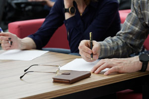 Two people at a table, writing on papers, with glasses and a wallet nearby, representing divorce discussions